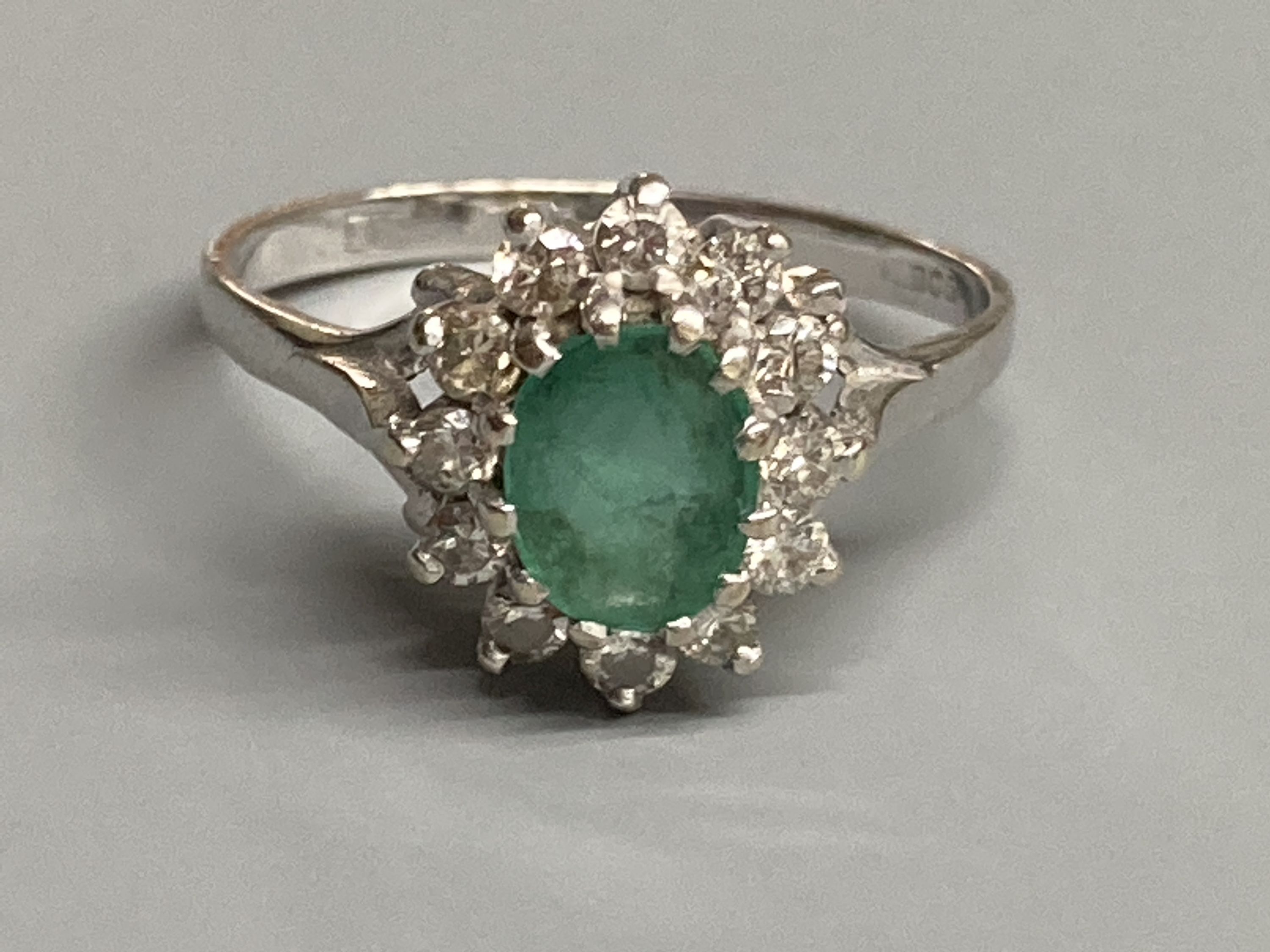 A modern 18ct white gold, emerald and diamond set oval cluster ring, size O/P, gross 3.6 grams.